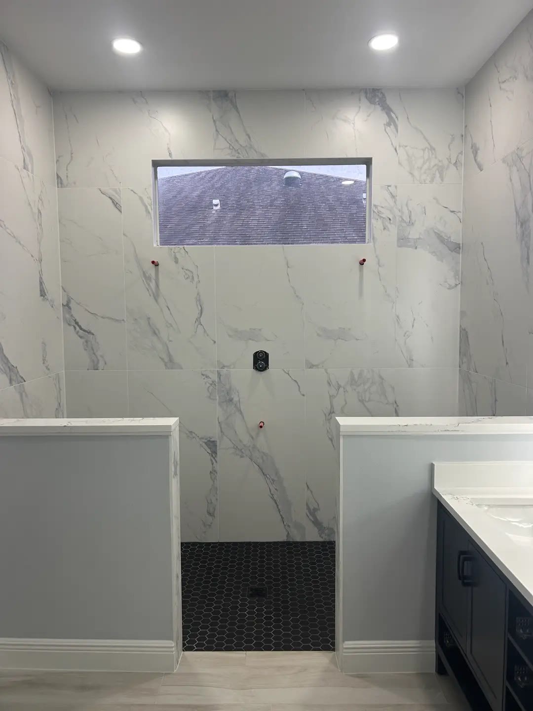 A Brevard County walk-in shower with large marble-look tile and a hexagon tile floor, tiled and ready for fixtures and glass
