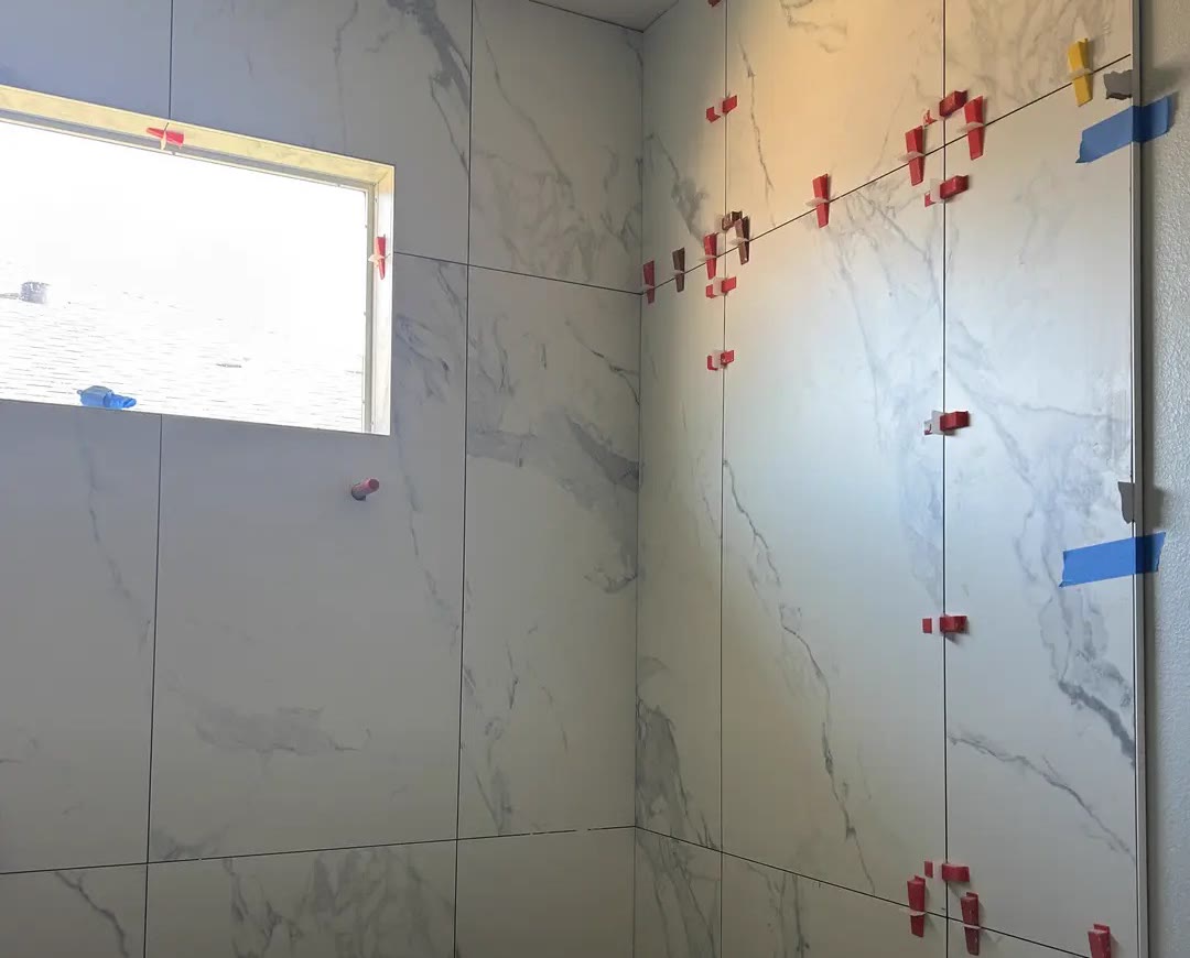 Large marble-look wall tile being set in a shower, with leveling clips still in place